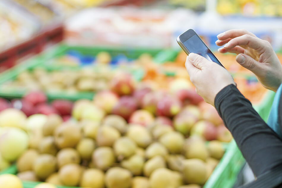 person holding their phone in front of produce section at grocery store