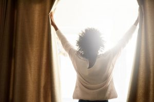 Woman opening curtains to let sunshine in.